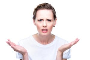 portrait of young woman with confused look shrugging her shoulders in front of white background