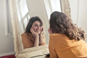 woman looking in mirror smiling at herself after healing from oral surgery