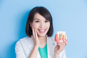 woman touching her face and holding model of dental implant