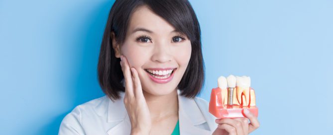 woman touching her face and holding model of dental implant