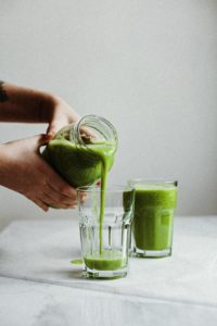 hands pouring a green smoothie into a glass which is one of the foods to eat after wisdom teeth removal