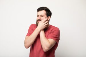 man in red shirt holding his face because of wisdom teeth removal pain