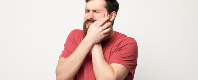 man in red shirt holding his face because of wisdom teeth removal pain