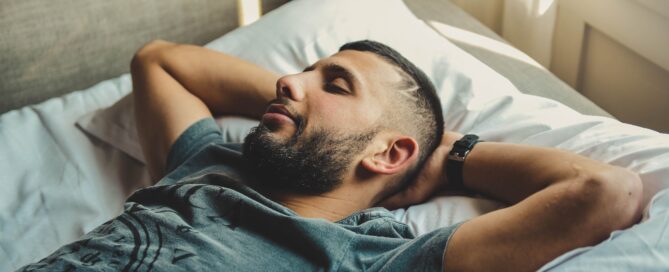 man sleeping on bed with hands behind his head